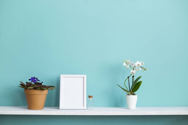 Décoration de chambre moderne avec cadre photo maquette. Etagère blanche contre le mur turquoise pastel avec orchidée en pot et plante violette
. - Photo, image
