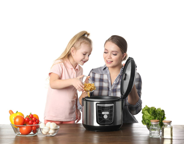 Mother and daughter preparing food with modern multi cooker at table against white background - Foto, immagini