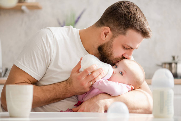 Młody ojciec całuje swoje dziecko podczas picia mleka - Zdjęcie, obraz