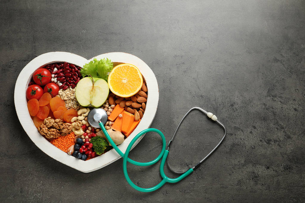 Heart shaped tray with healthy products and stethoscope on grey background, top view. Space for text - Fotó, kép
