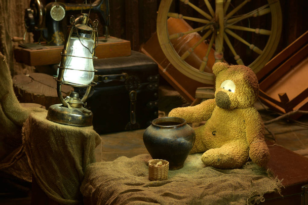 stacked in the attic of a dwelling house old things including a toy bear, a lamp, a sewing machine, a chest, a jug and a big wheel. - Photo, Image