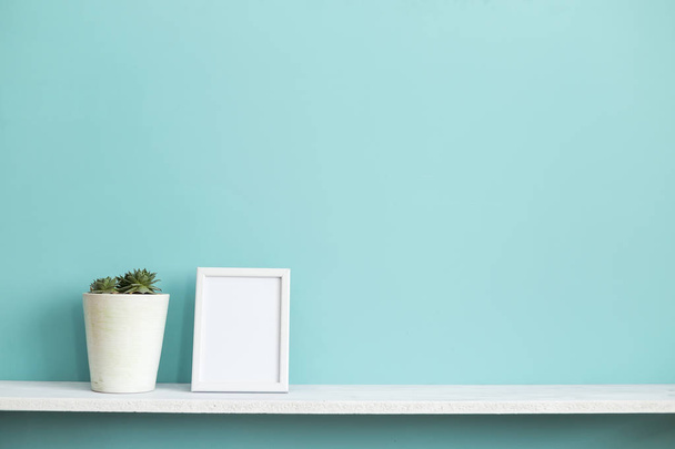 Moderne kamer decoratie met Picture Frame mockup. Witte plank tegen pastel Turquoise muur met ingegoten succulente installatie. - Foto, afbeelding
