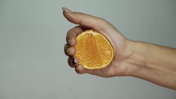 girl squeezes out juice from half an orange with her hand - Felvétel, videó