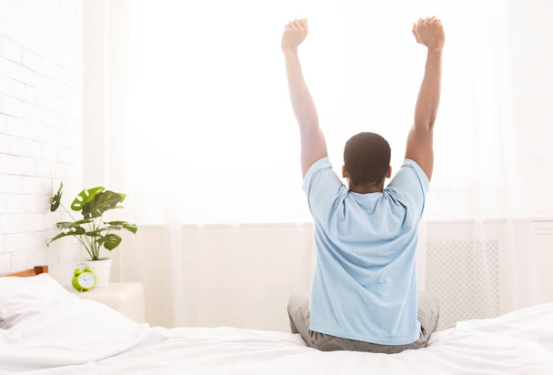Young man waking up in bed and stretching his arms - Foto, Bild