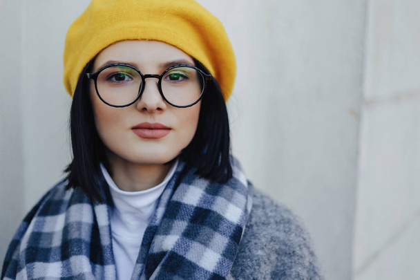 Muchacha atractiva en gafas de abrigo y boina amarilla sobre un fondo claro simple
 - Foto, Imagen