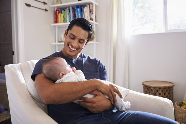 Proud Hispanic father sitting and holding his four month old son in arms, horizontal - Photo, Image