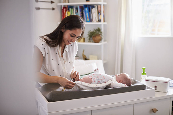 Happy mother changing the diaper of her newborn son at home on changing table, selective focus - Фото, зображення