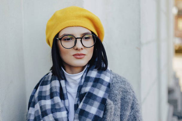 Muchacha atractiva en gafas de abrigo y boina amarilla sobre un fondo claro simple
 - Foto, Imagen