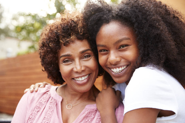 Middle aged black mum and teenage daughter embracing and smiling to camera - Fotografie, Obrázek