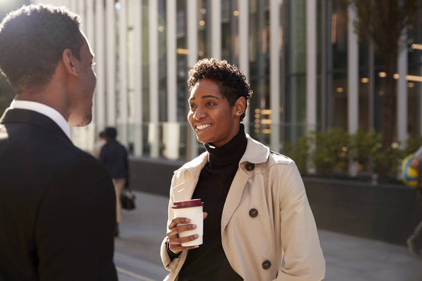 Young black businesswoman standing on the street with a takeaway coffee, talking to her male colleague, selective focus - Фото, изображение