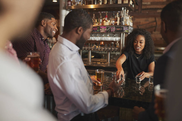 Barmaid Serving Shots To Group Of Male Friends On Night Out In Bar - Foto, immagini