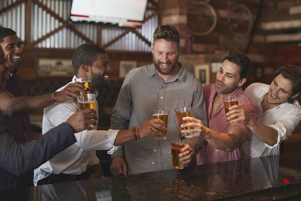 Group Of Male Friends On Night Out For Bachelor Party In Bar Making Toast Together - 写真・画像