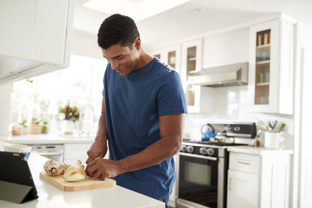 Widok z boku dorosłego człowieka stojącego na blacie kuchennym przygotowując jedzenie za pomocą przepisu na komputerze typu Tablet, zbliżenie, selektywne skupienie - Zdjęcie, obraz