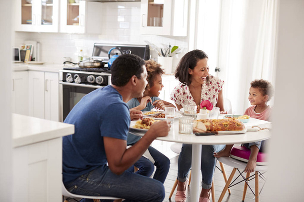 Young mixed race family eating a meal together at the table in their kitchen, seen from doorway - Foto, Bild