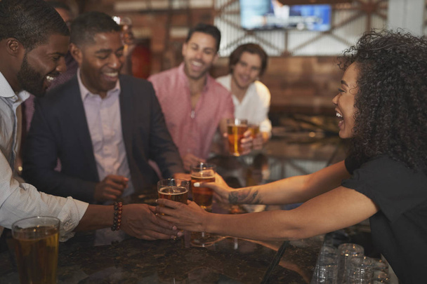 Barmaid Serving Group Of Male Friends On Night Out For Bachelor Party Making Toast Together - Photo, image