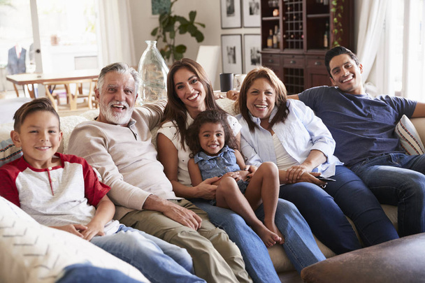 3 γενιά ισπανόφωνων οικογένεια κάθεται στον καναπέ βλέποντας τηλεόραση, κοιτάζοντας την κάμερα - Φωτογραφία, εικόνα