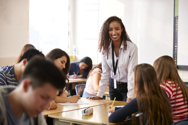 Portrait Of Smiling Female High School Teacher Standing By Student Table Teaching Lesson - Foto, immagini