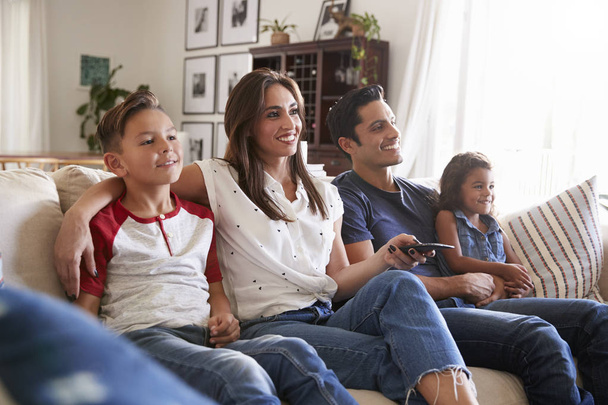 Young Hispanic family sitting on the sofa at home watching TV together, close up - Foto, Imagen