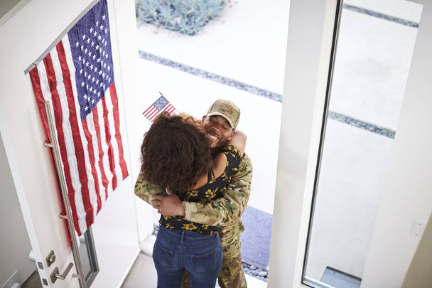 Podwyższony widok powracającego czarnego męskiego żołnierza obejmującego żonę w drzwiach domu - Zdjęcie, obraz