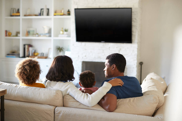 Vue arrière de la jeune famille assise sur le canapé et regardant la télévision ensemble dans leur salon
 - Photo, image