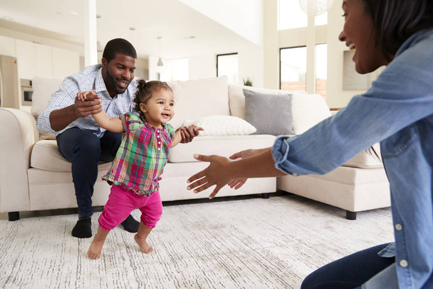 Family At Home Encouraging Baby Daughter To Take First Steps - Fotó, kép