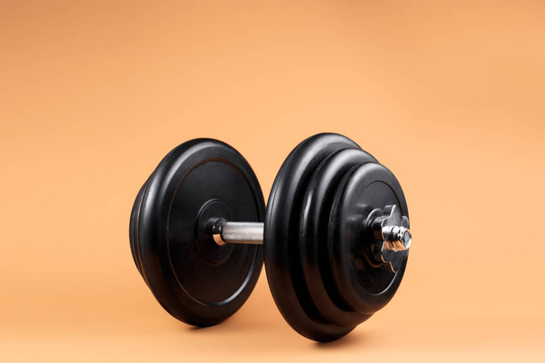 Professional dumbbell and weight plates over beige background. Black metal dumbbell with chrome silver handle. Gym equipment. Fitness concept. - Fotografie, Obrázek