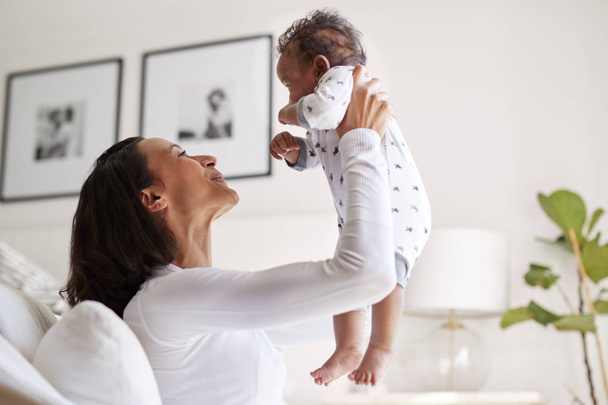 Happy mixed race young adult mother raising her three month old baby son in the air - Photo, Image