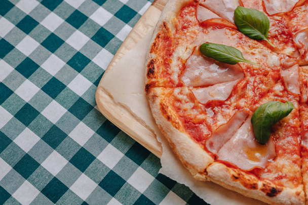 Неаполитанская пицца с ветчиной, сыром, аругулой, базиликом, помидорами, посыпанными сыром на деревянную доску на скатерти в камере с местом для текста
 - Фото, изображение