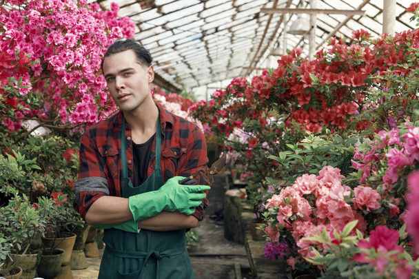 Hermoso joven guapo en ropa de trabajo con peinado de moda en guantes de jardín verdes
 - Foto, imagen