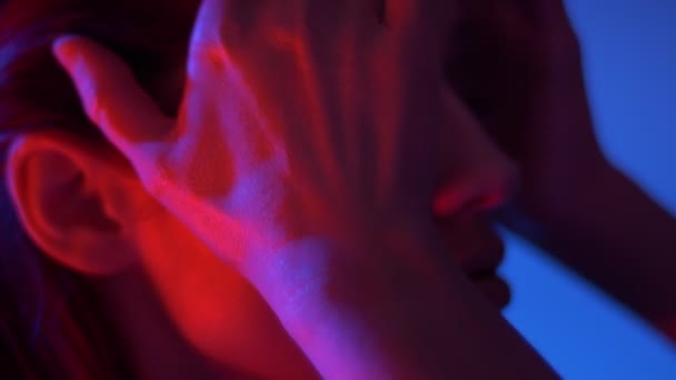 Close-up portrait in profile of fantastic fashion model in red neon lights runs hands through her hair. - Séquence, vidéo