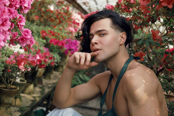 Attractive muscular florist with naked torso sitting among colorful flowers - 写真・画像