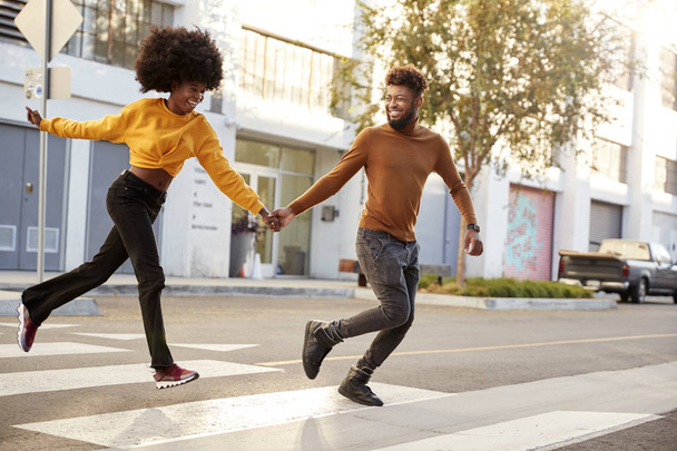 Fashionable young black couple running across a city street holding hands, full length, close up - Foto, Bild