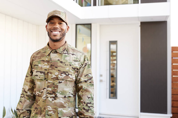 Millennial soldier in camouflage uniform standing outside modern house smiling to camera, close up - Foto, Imagem
