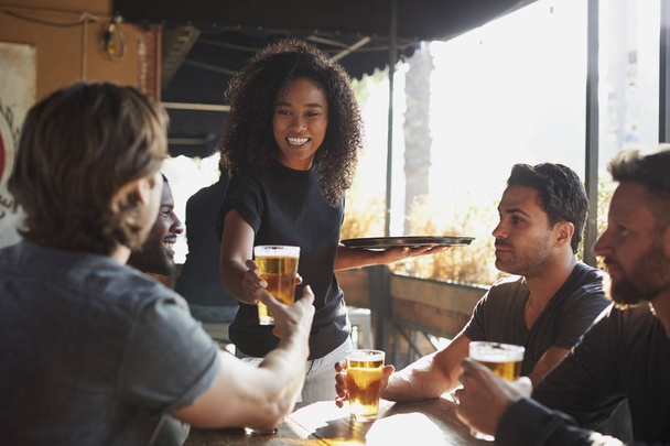 Waitress Serving Drinks To Group Of Male Friends Meeting In Sports Bar - Foto, imagen
