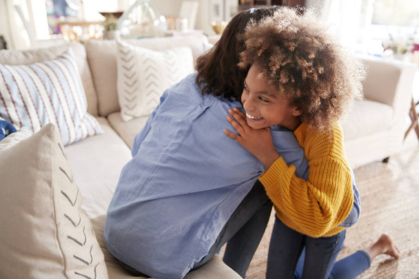 Pre-teen girl hugging her mother sitting on sofa in the living room, elevated, back view - Fotó, kép