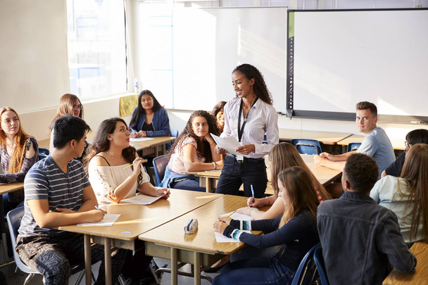 Female High School Teacher Standing By Student Table Teaching Lesson - Foto, imagen