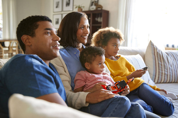Young family sitting together on the sofa in their living room watching TV, selective focus - Photo, image