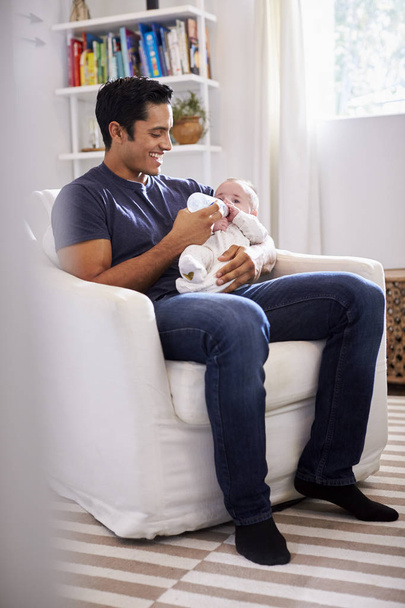 Smiling Hispanic father holding his four month old son feeding him a bottle, full length, vertical - Fotografie, Obrázek