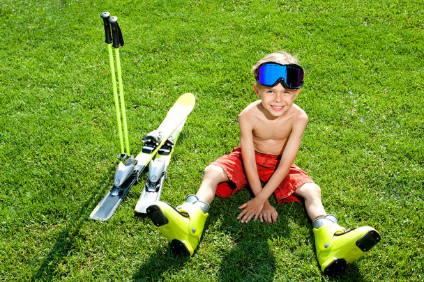 Portrait of attractive child sitting on grass with ski - Photo, Image