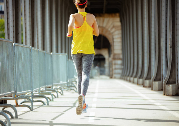 Seen from behind active sports woman in fitness clothes on Pont de Bir-Hakeim bridge in Paris jogging. - Фото, изображение