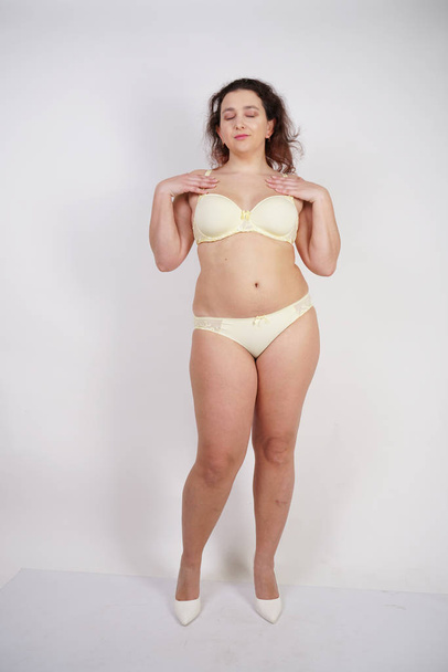 csinos pufby lány visel divatos sárga fehérnemű és szereti a testét és magát. kövér nő fehérnemű fehér alapon. - Fotó, kép