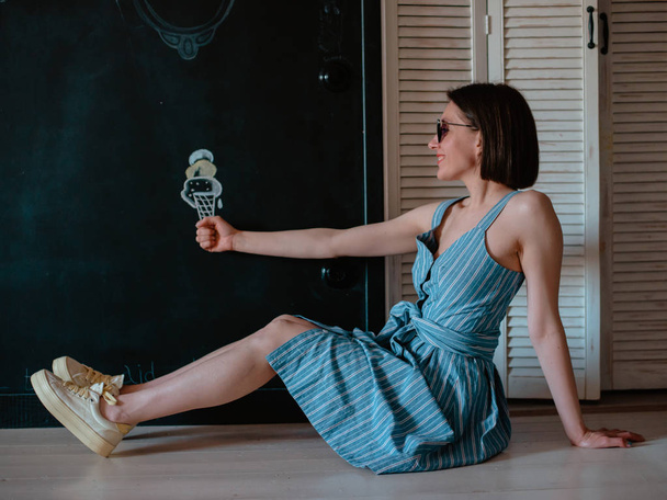 een jong sexy meisje in een korte jurk in zonnebril houdt een geschilderd ijs op de muur. - Foto, afbeelding
