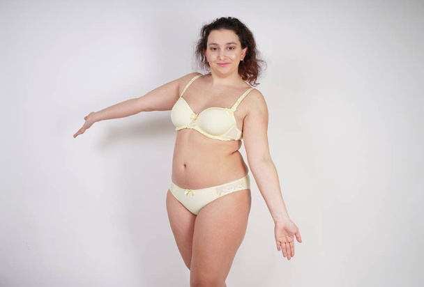 pretty chubby girl wearing fashionable yellow underwear and loves her body and herself. plump woman in lingerie on white background. - Photo, Image