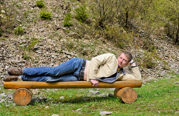 Jovem loiro deitado de lado em um banco
 - Foto, Imagem
