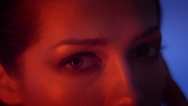 Close-up Eye-portret van kalm mode model in rode neon licht te kijken bewaring met geen emoties in de camera. - Video