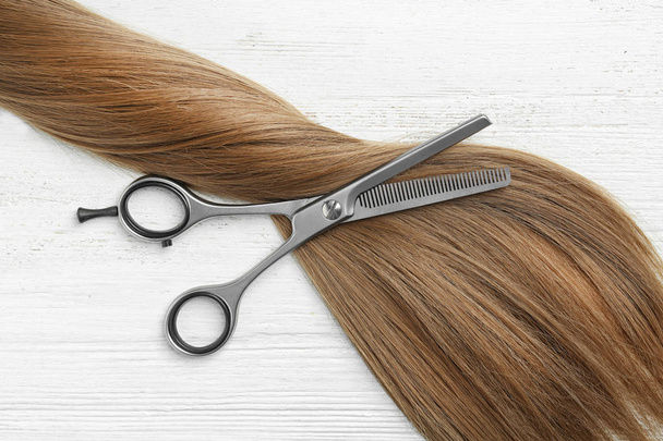 Flat lay composition with light brown hair and thinning scissors on white wooden background. Hairdresser service - Photo, image