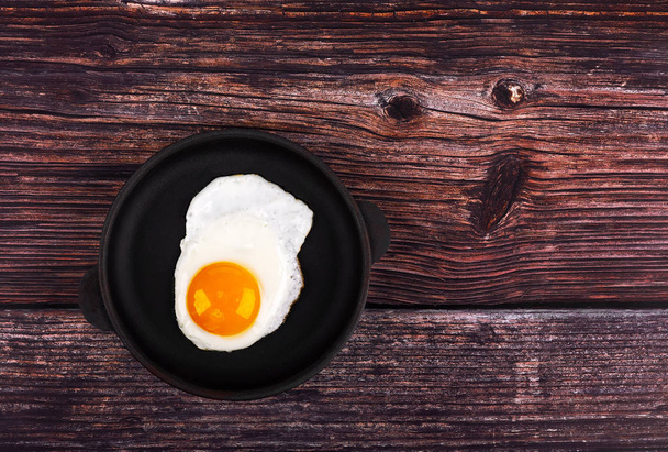 Τηγανητό αυγό στο τηγάνι, σε ξύλινο φόντο. Κορυφαία προβολή. - Φωτογραφία, εικόνα