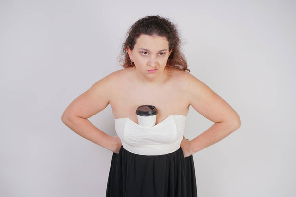 chubby woman with a paper Cup of coffee stands and is disgusted with the drink, showing the emotions of the negative. plump girl hates coffee. - Photo, Image