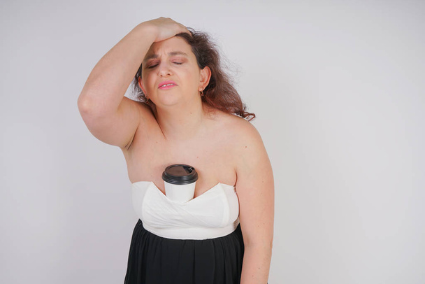 femme dodue avec une tasse de papier de café dans sa main souffre de maux de tête et de fatigue. chubby fille debout sur fond blanc dans Studio
 - Photo, image