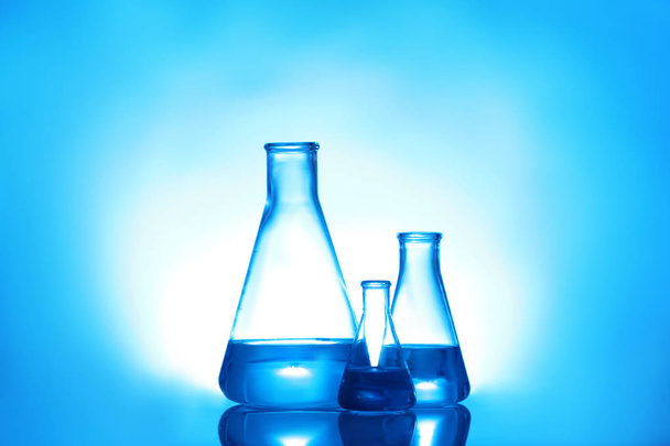 色の背景に液体が付いている実験室のガラス製品。ソリューション化学 - 写真・画像